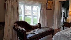 A room with a large window, a leather armchair, a bed, and a lamp. - Carrick's At Castle Farm (Dereham)
