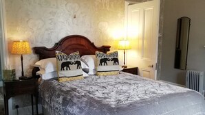 A bedroom with a large bed, two bedside lamps, a wooden headboard, patterned wallpaper, a mirror, and a radiator. - Carrick's At Castle Farm (Dereham)
