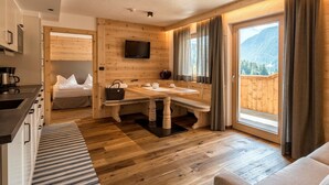 A cozy room with a wooden interior, a dining table, a sofa, and a large window with curtains. - Residence Cesa Sassela (Ortisei)