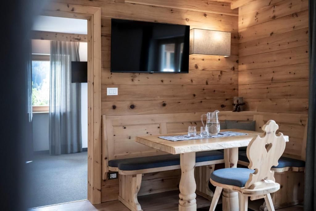 En inredning med träpaneler, en tv som är monterad på väggen, ett bord med stolar och en bänk.