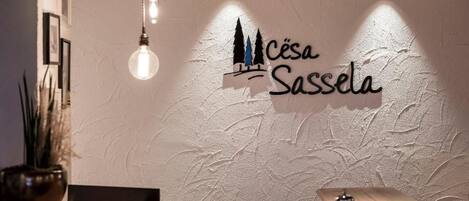 A reception desk with a logo above it, a hanging light fixture, and a potted plant to the left.