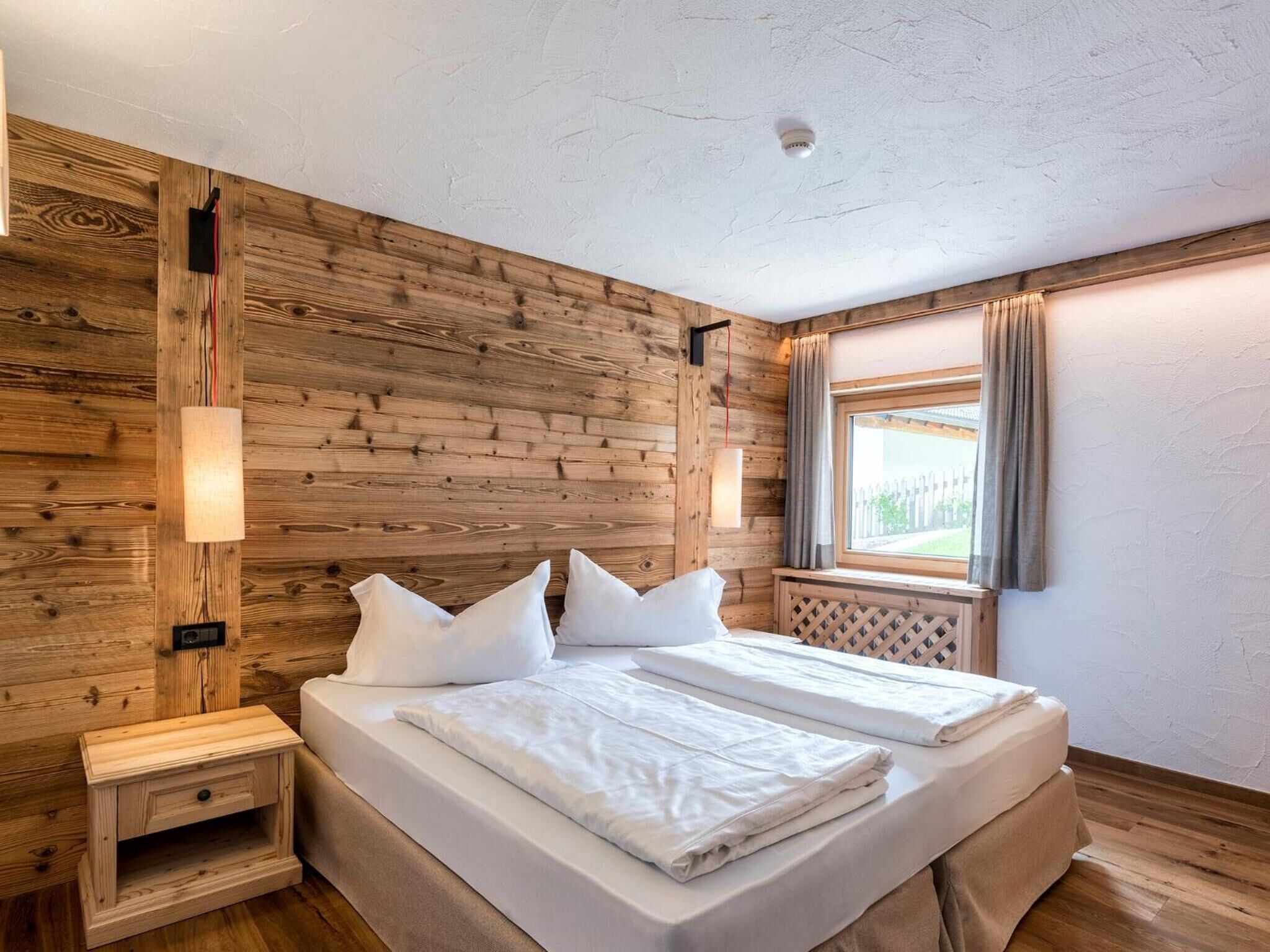 Une chambre aux murs lambrissés, avec un lit, des tables de chevet et une fenêtre avec des rideaux.