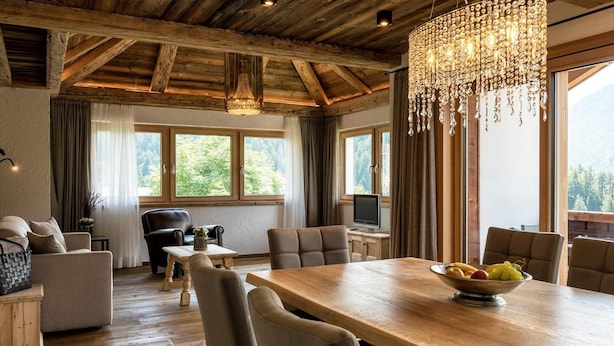 A spacious room with a wooden ceiling, a chandelier, a dining table with chairs, a sofa, and a TV. - Residence Cesa Sassela (Ortisei)
