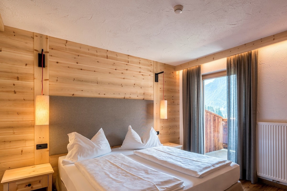 Ein Hotelzimmer mit Holzwand, einem Bett mit weißer Bettwäsche, zwei Nachttischen und einem Fenster mit Vorhängen.