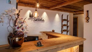 A wooden reception desk with a vase of orchids, a clock, and a sign reading "Sassela". - Residence Cesa Sassela (Ortisei)