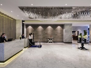 Zona de recepción de hotel con un mostrador de mármol, una lámpara moderna y una mesa de recepción.