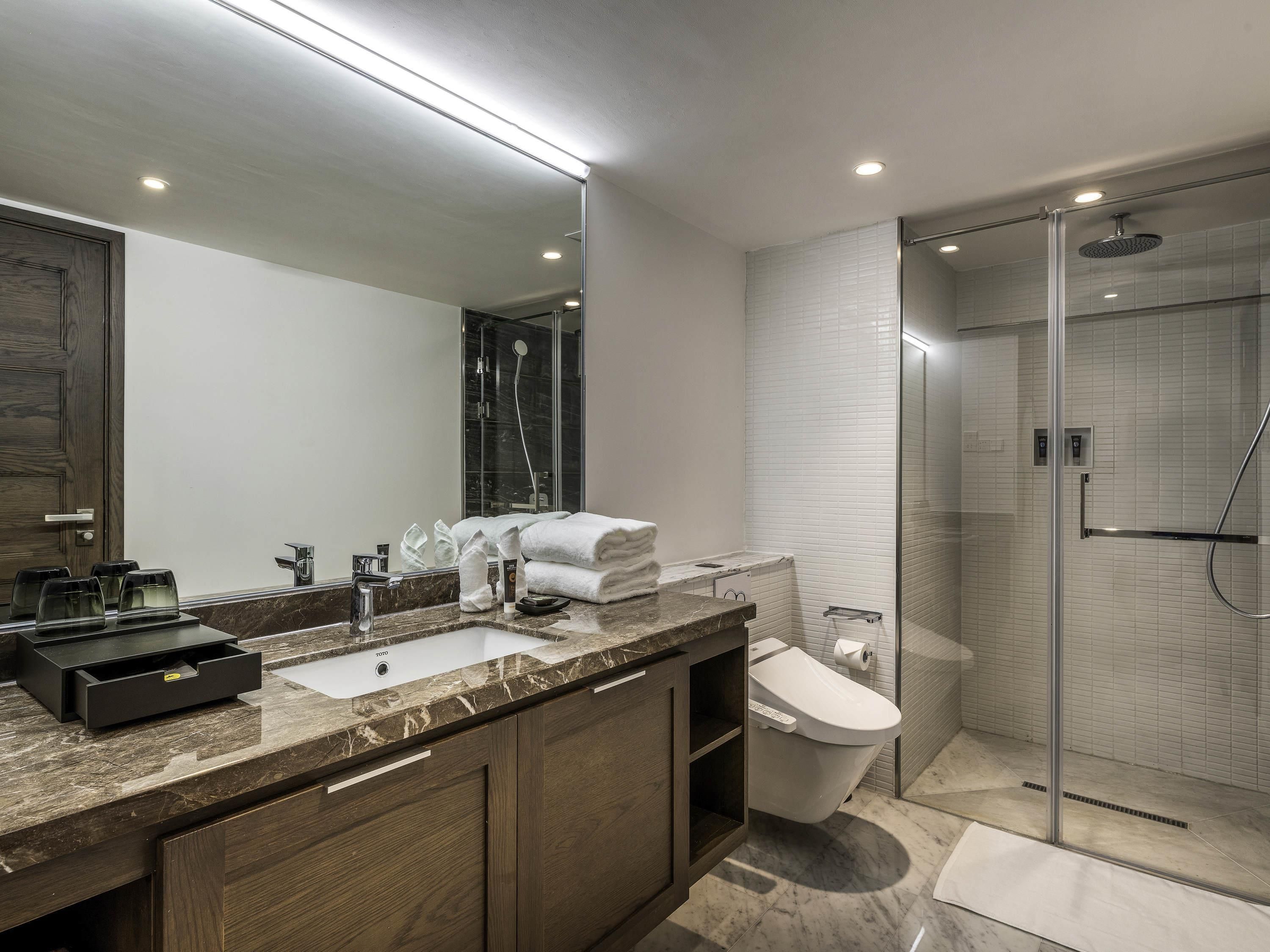 A modern bathroom with a marble countertop, a glass-enclosed shower, and a toilet.