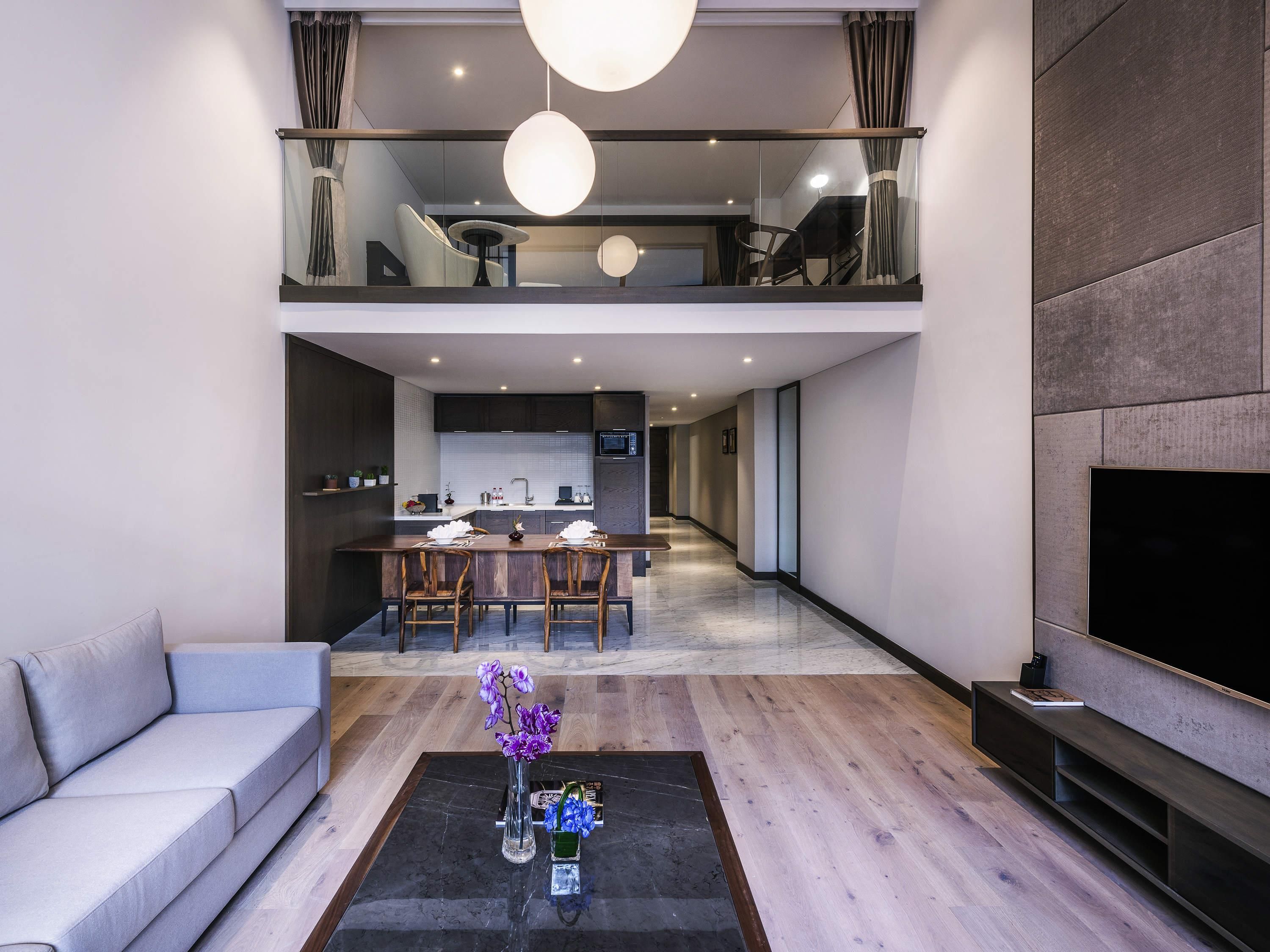 Una sala moderna con un sofá, una mesa de centro con jarrones, un comedor con sillas y una cocina al fondo.