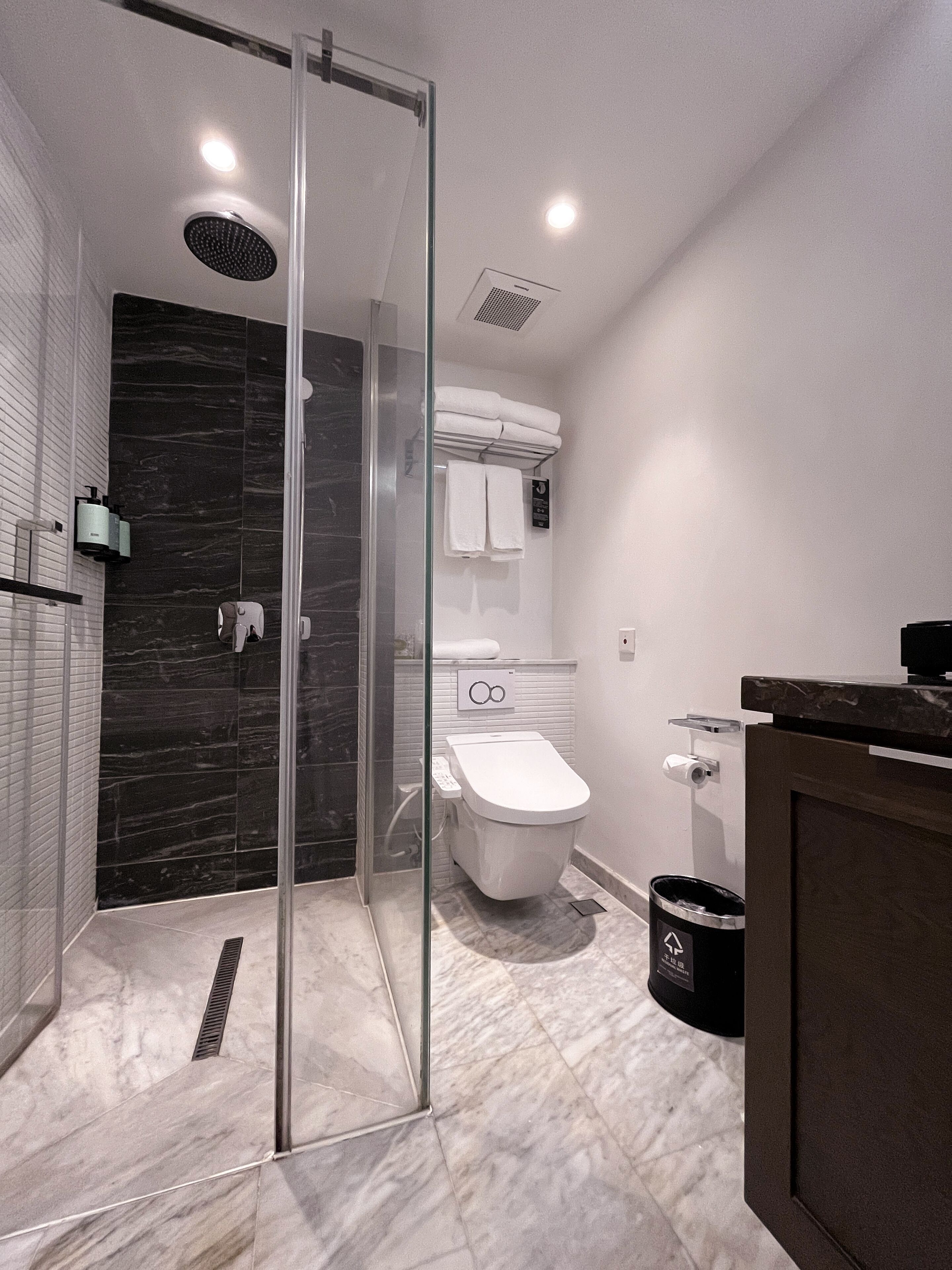 Un baño moderno con ducha envuelta en vidrio, inodoro y un cesto de basura.