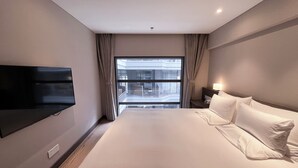 A hotel room with a large bed, a flat-screen TV mounted on the wall, a bedside table with a lamp, and a view of a building through the window. - Novotel Suites Shanghai Hongqiao Hotel (Shanghai)