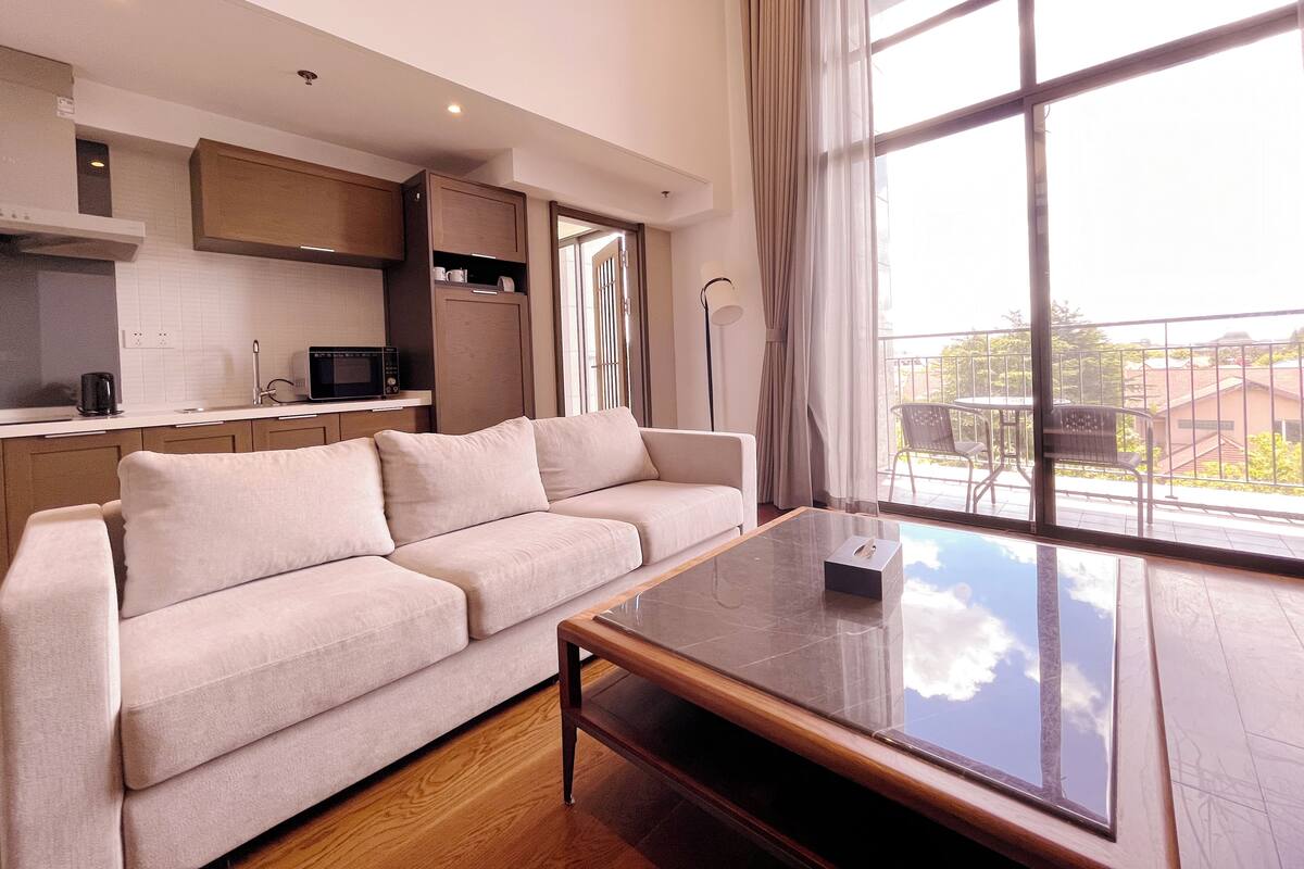 Una sala de estar moderna con un sofá, una mesa de centro y vistas al exterior a través de amplios ventanales.