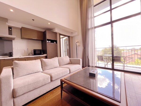 Un salon moderne avec un canapé, une table basse et une vue sur l’extérieur grâce à de grandes fenêtres.