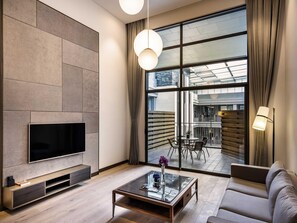 A modern living room with a flat-screen TV, a glass coffee table, a sofa, and a dining area visible through large windows.