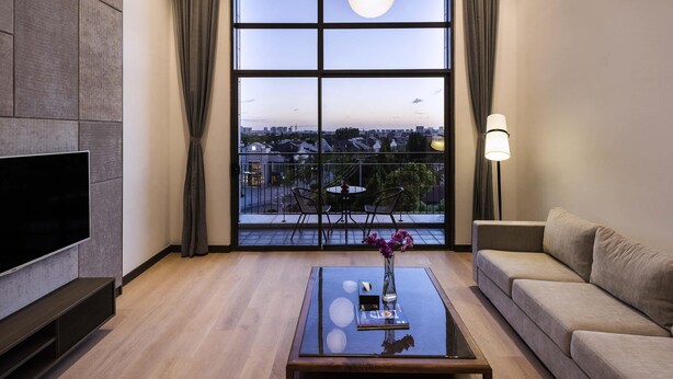 Un salon moderne doté d’une grande fenêtre, d’un téléviseur à écran plat, d’un canapé, d’une table basse et d’un luminaire suspendu.