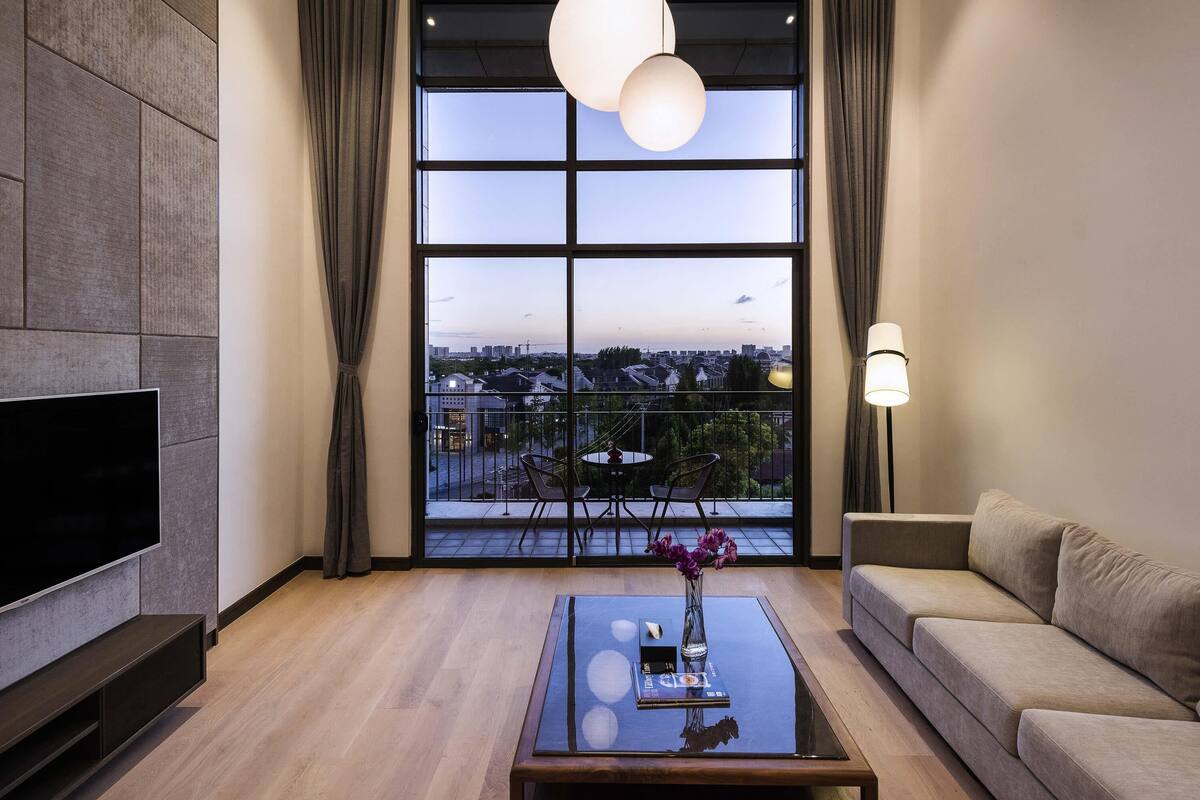 Una sala de estar moderna con un gran ventanal, un televisor de pantalla plana, un sofá, una mesa de centro e iluminación colgante.