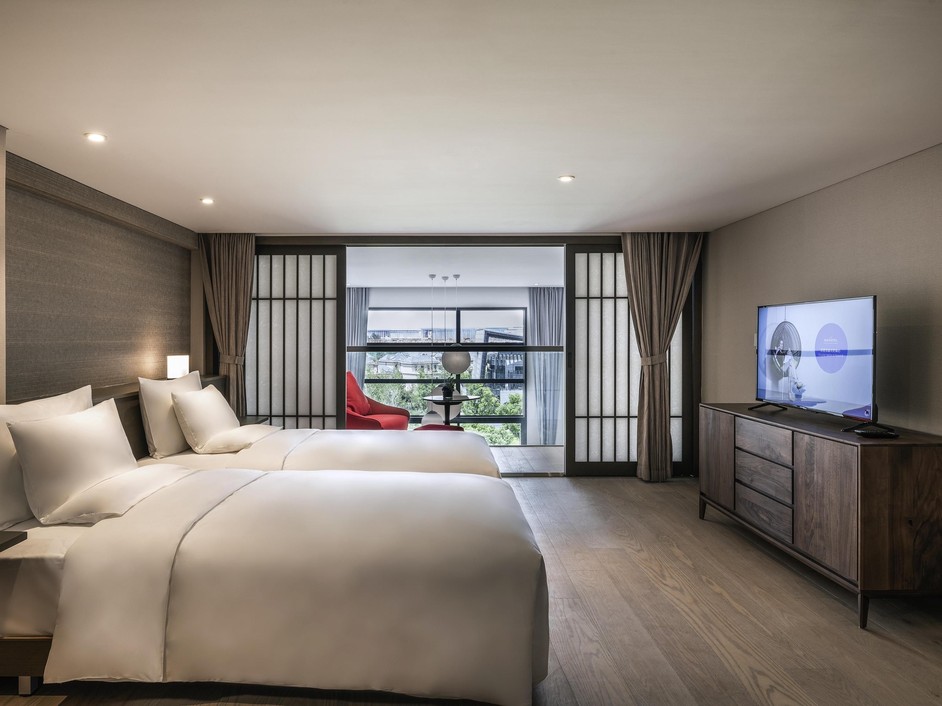Ein modernes Hotelzimmer mit einem großen Bett, einem Fernseher und Blick auf die Stadt.