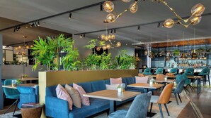 Un área de bar moderna con diferentes disposiciones de asientos, incluyendo sofás y mesas, y una barra con diversos tipos de botellas.