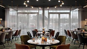 Un comedor moderno con mesas redondas, sillas y un amplio ventanal con cortinas ligeras.