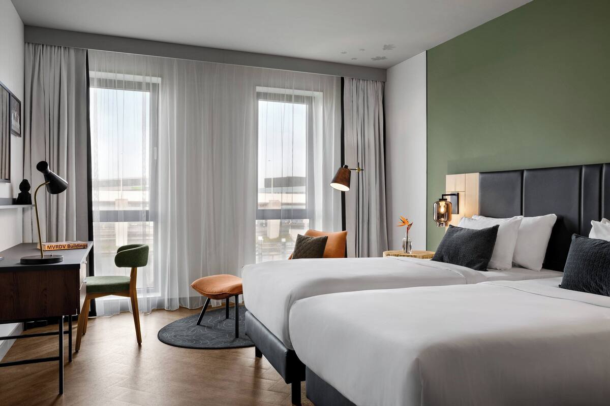 Habitación de hotel con dos camas, un escritorio, una silla y vista a la ciudad.