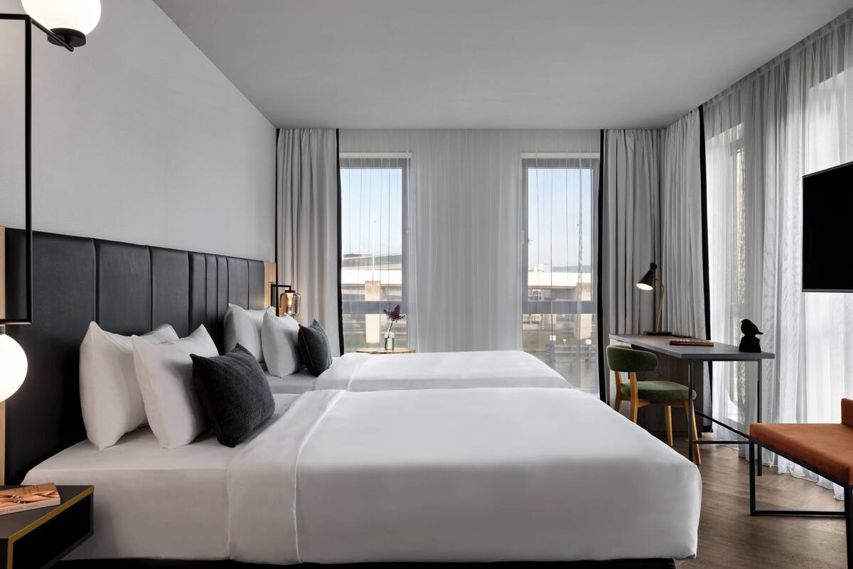 Habitación de hotel con dos camas, un escritorio, una silla y un televisor.