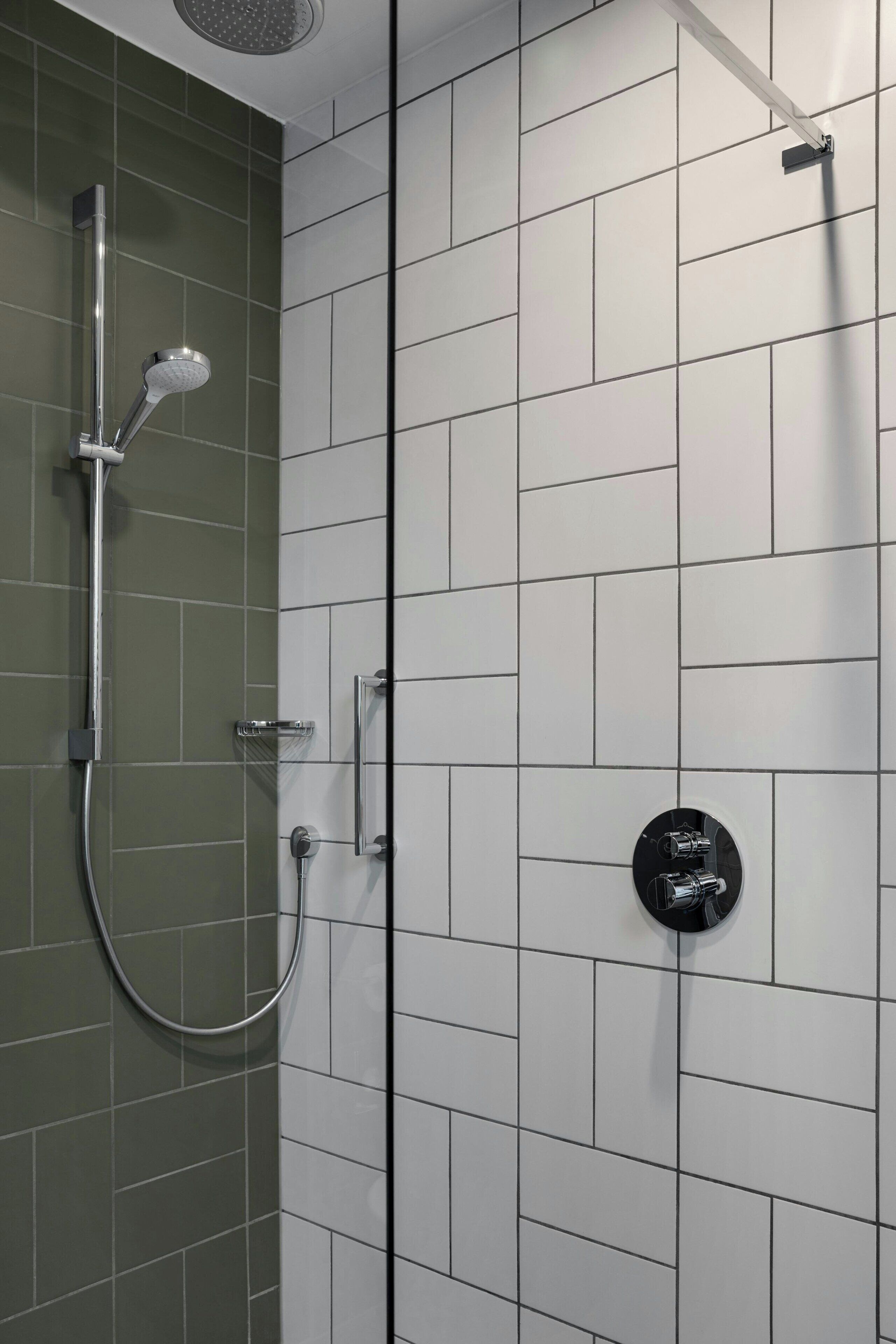 A shower with a handheld showerhead and a wall-mounted control panel.