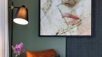 Una habitación moderna con un cuadro abstracto grande, una mesa redonda de madera con un jarrón de flores y un sillón naranja cómodo.