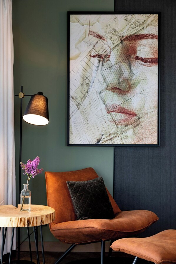Una habitación moderna con un cuadro abstracto grande, una mesa redonda de madera con un jarrón de flores y un sillón naranja cómodo.
