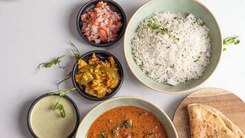Diversas especias y platos, incluyendo un bol de curry, arroz y pan plano, dispuestos sobre una superficie blanca.