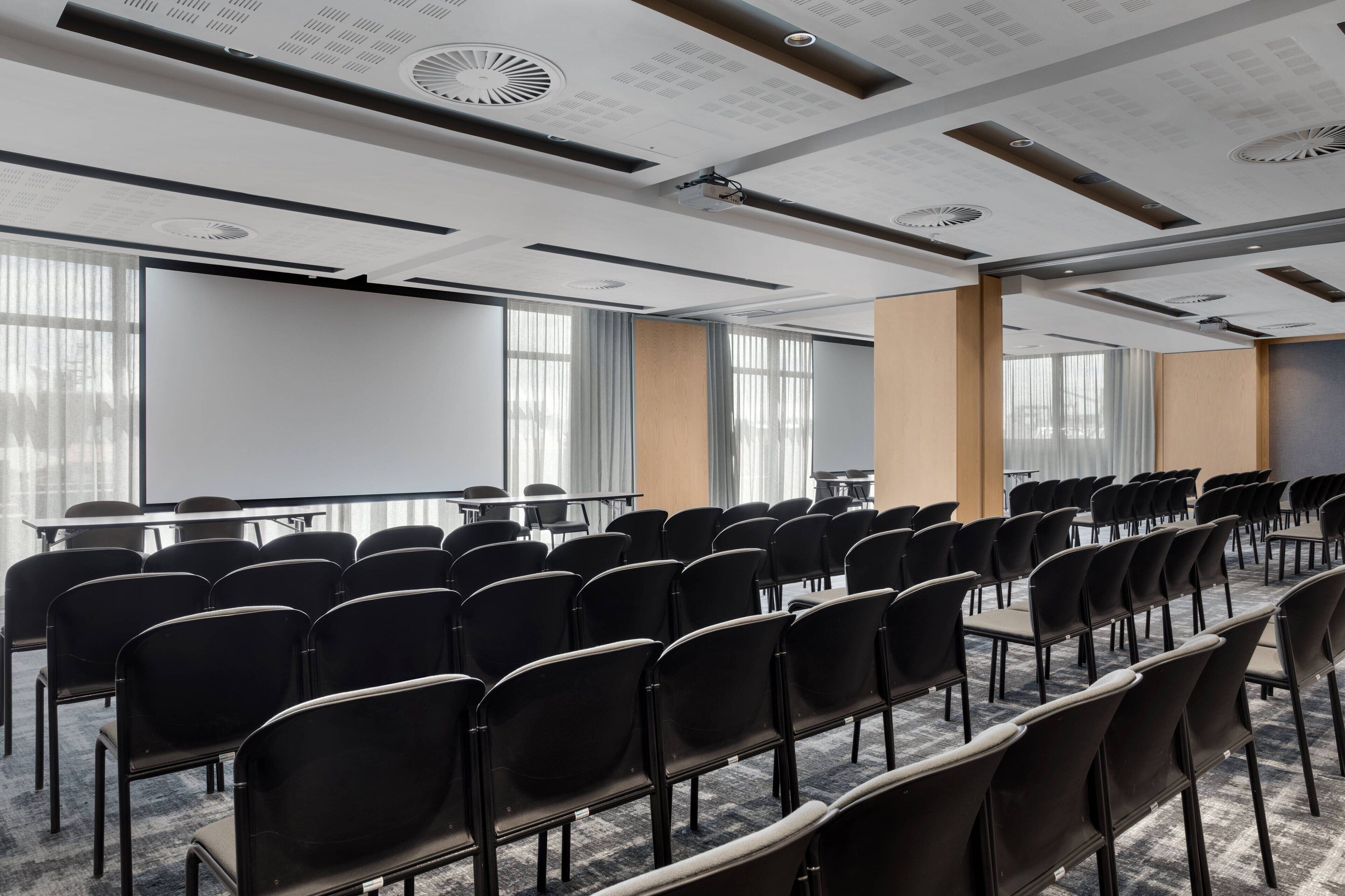 A conference room with rows of black chairs, a projector screen, and large windows.