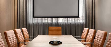 A conference room with a long table, leather chairs, a projector screen, and a large window with curtains.