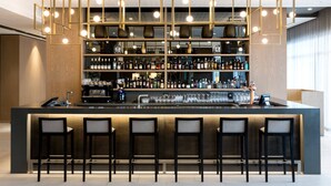 Um bar moderno com um balcão extenso, várias prateleiras de garrafas e uma luminária geométrica singular.