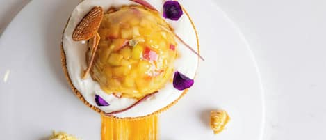 Un postre sobre un plato blanco con un hilo de salsa, una pequeña bola de helado y una flor decorativa.