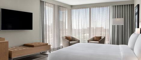Una habitación de hotel moderna con una cama grande, dos sillones, un televisor de pantalla plana y un escritorio con silla.