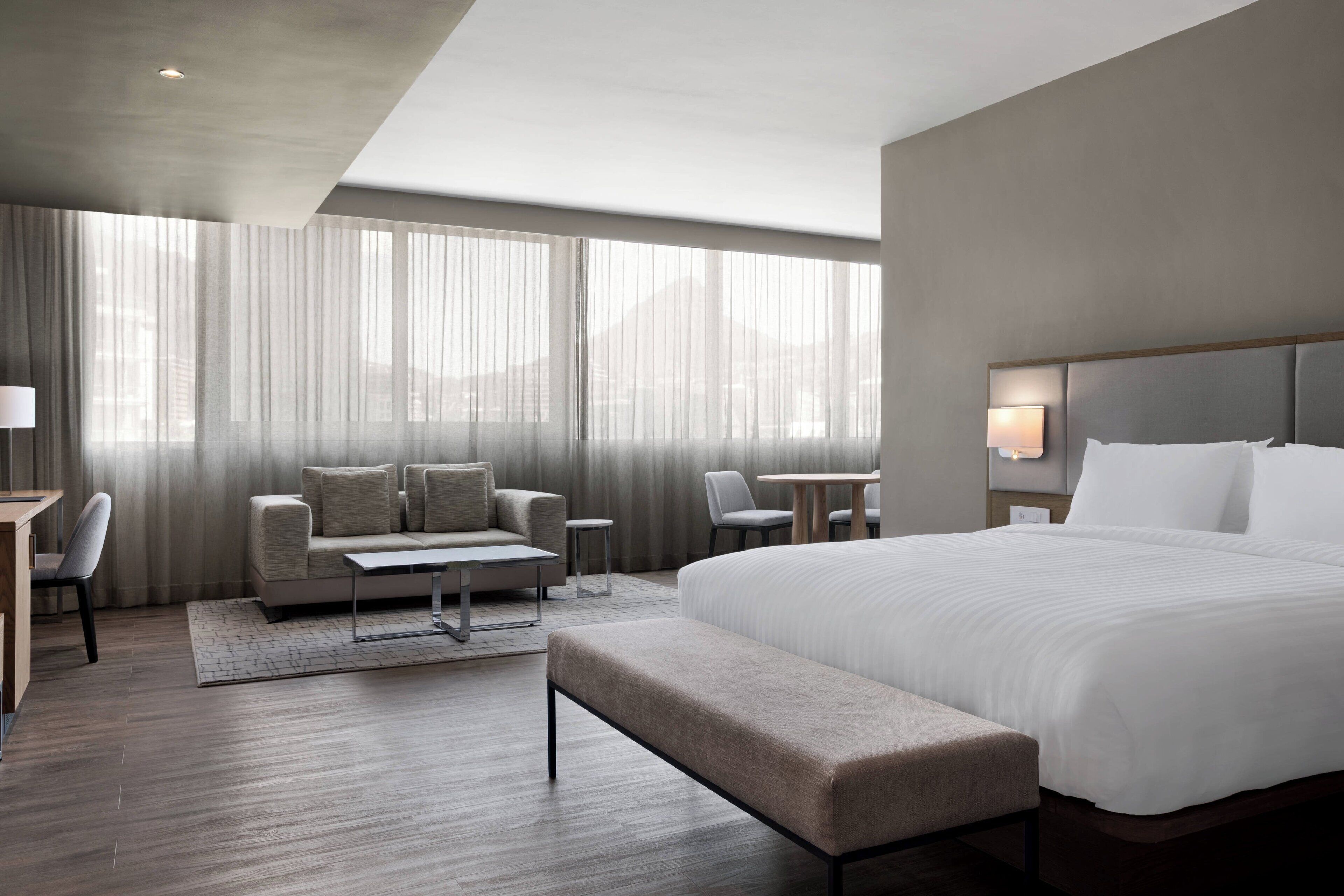 A modern hotel room with a large bed, a sofa, a small table, and a desk.
