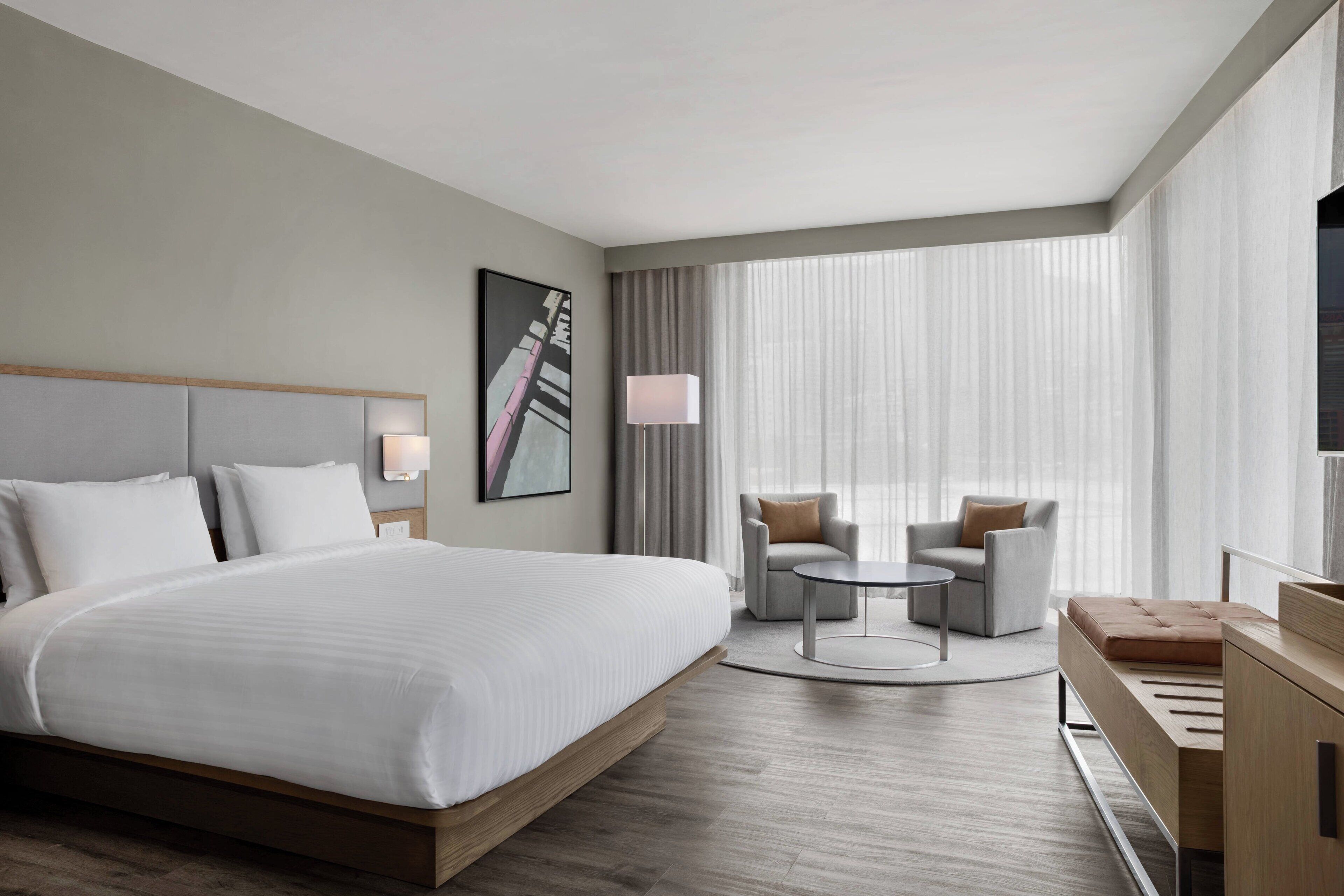 A modern hotel room with a large bed, two armchairs, a small round table, and a TV.