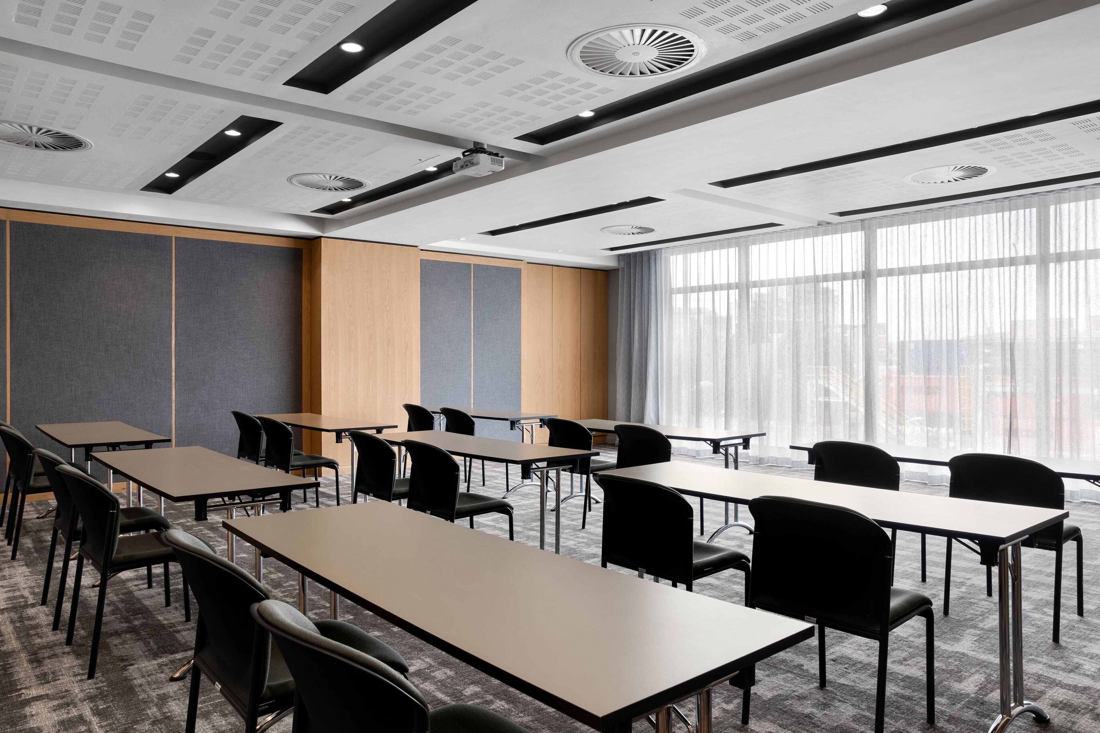 A conference room with multiple tables and chairs, large windows, and a ceiling with recessed lighting and ventilation.