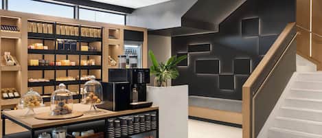 A modern interior with a coffee station, shelves with packaged goods, and a staircase.