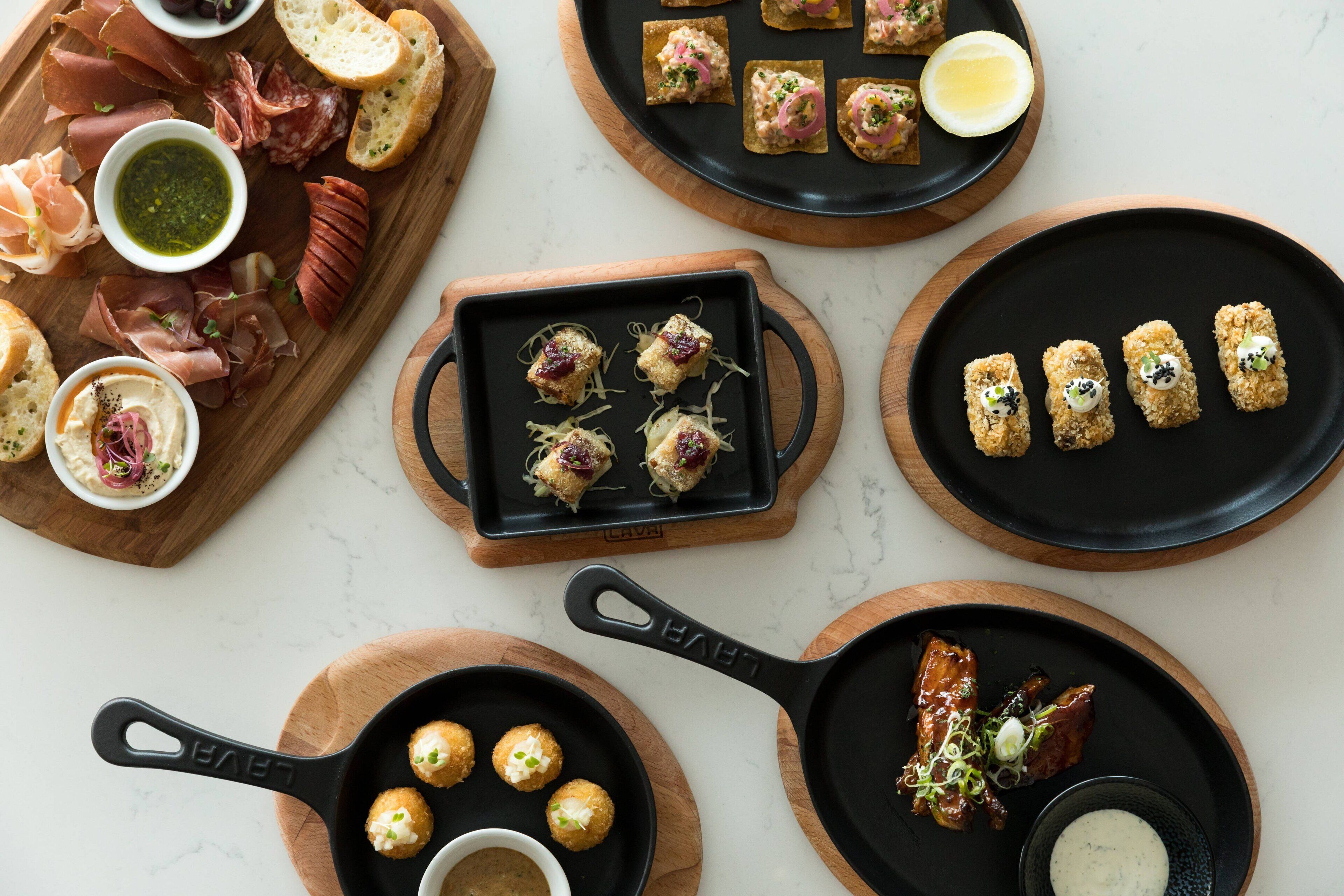 Diversos alimentos dispuestos en varios platos y una tabla de madera, incluyendo carnes, pan y guarniciones.