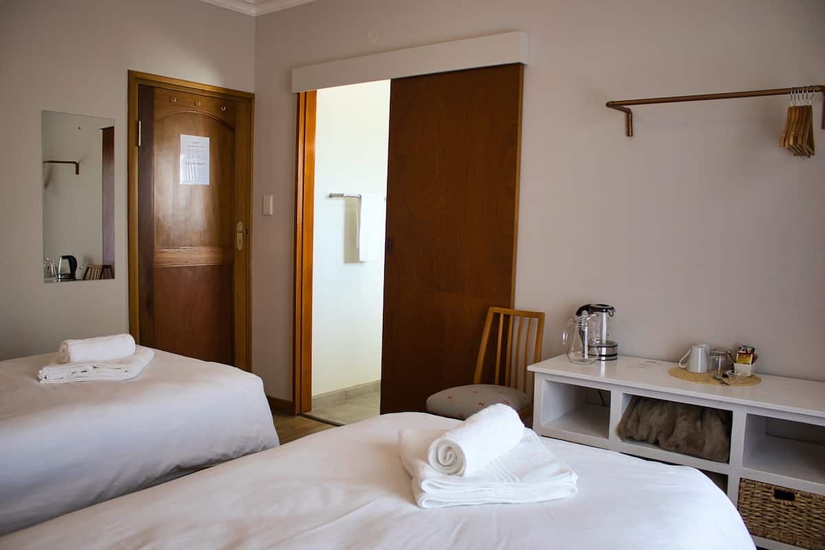 Een hotelkamer met twee bedden, een houten deur, een wit bureau met koffiezetapparaat en een spiegel aan de muur.