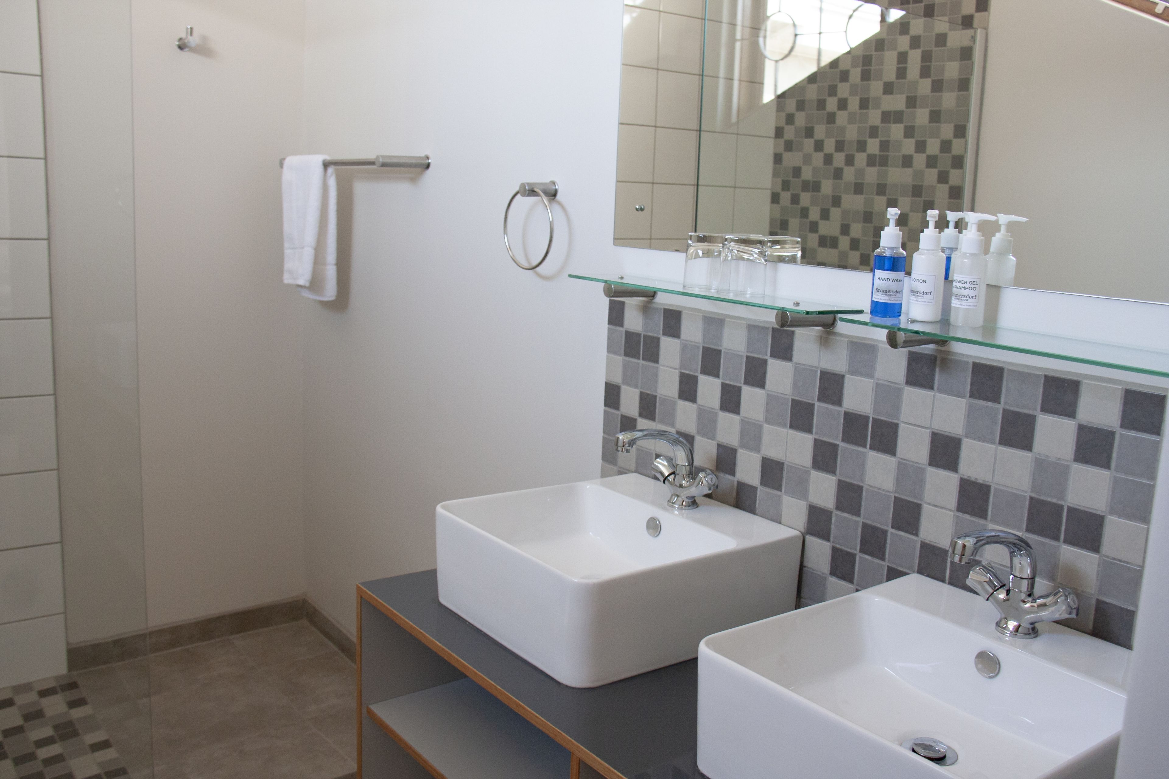 A bathroom with two sinks, a glass shelf with toiletries, a towel rack, and a shower area.