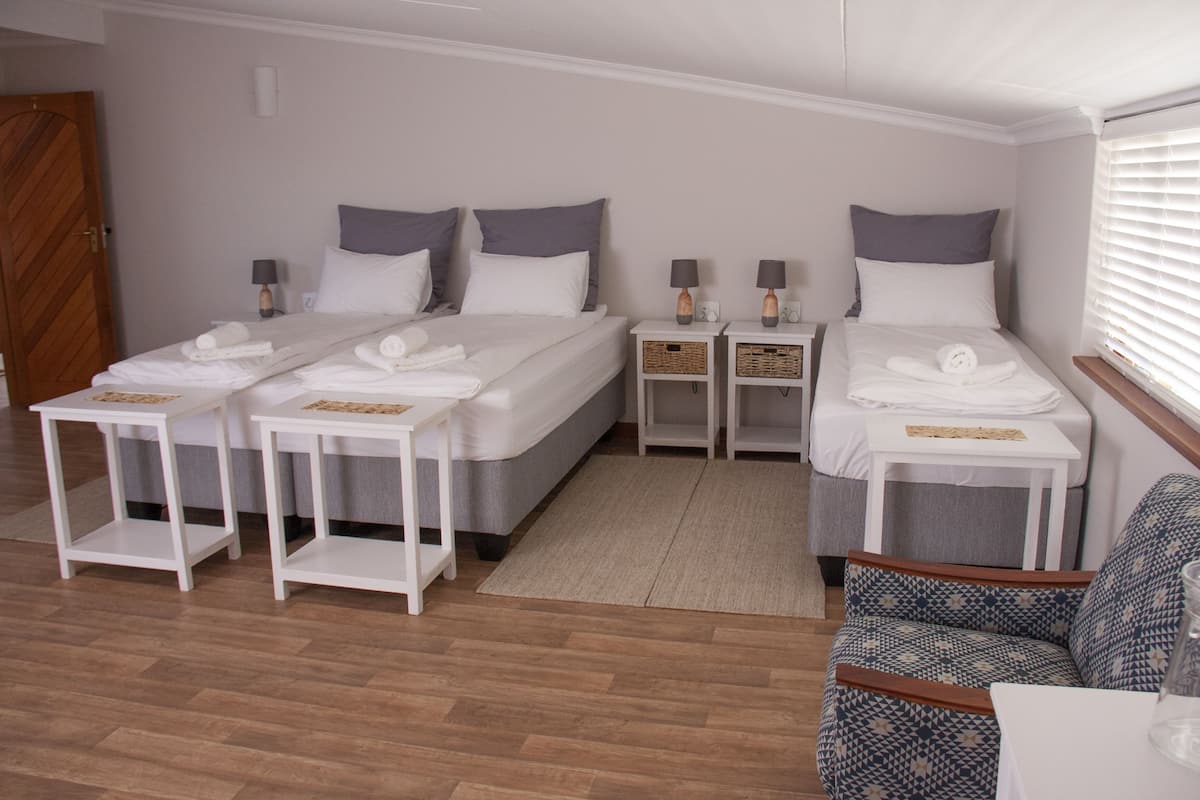 Een hotelkamer met twee bedden, elk voorzien van nachtkastje en lamp, een zithoekje met een gestreept fauteuil en een houten vloer.