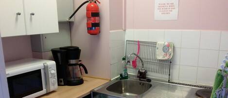 A compact kitchenette with a microwave, coffee maker, sink, and a fire extinguisher.