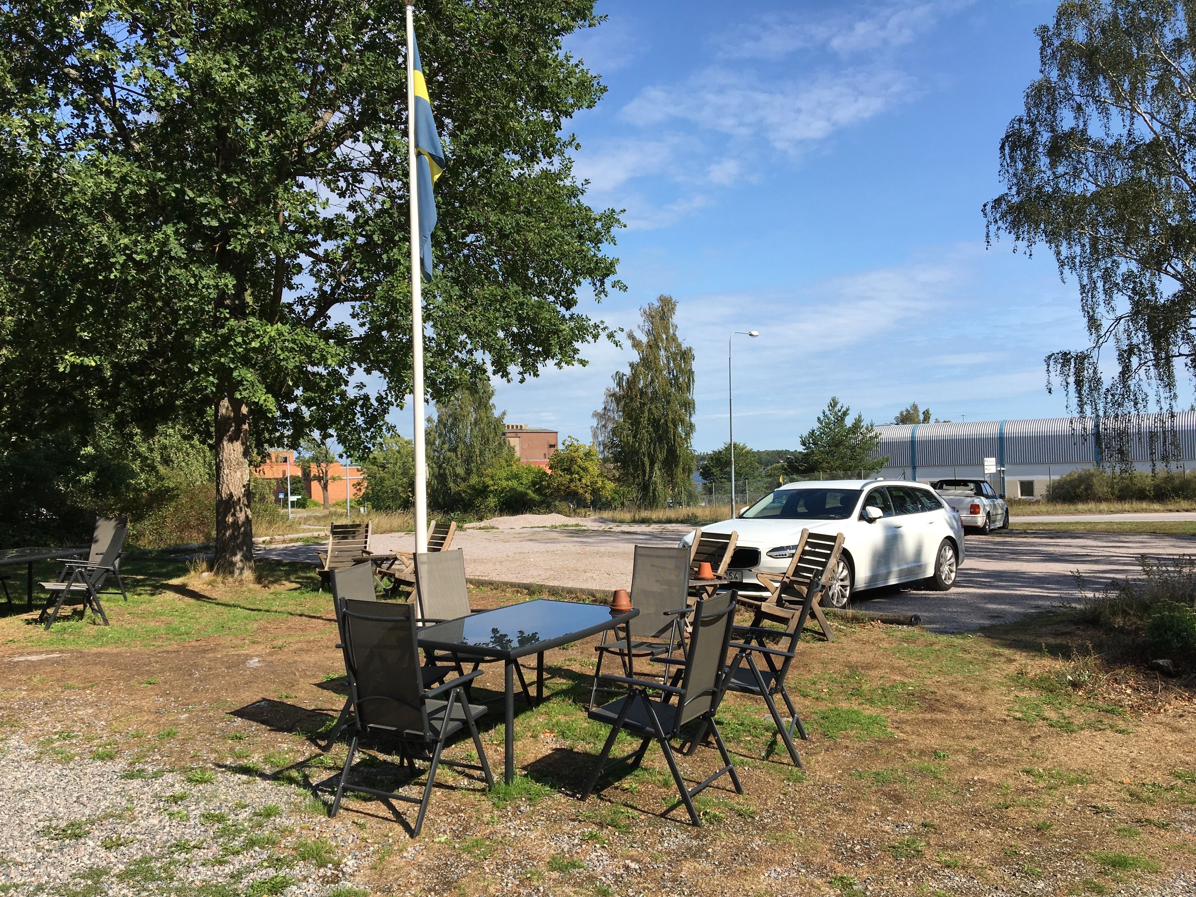 An outdoor seating area with a table and chairs, a flagpole, and a parked car.