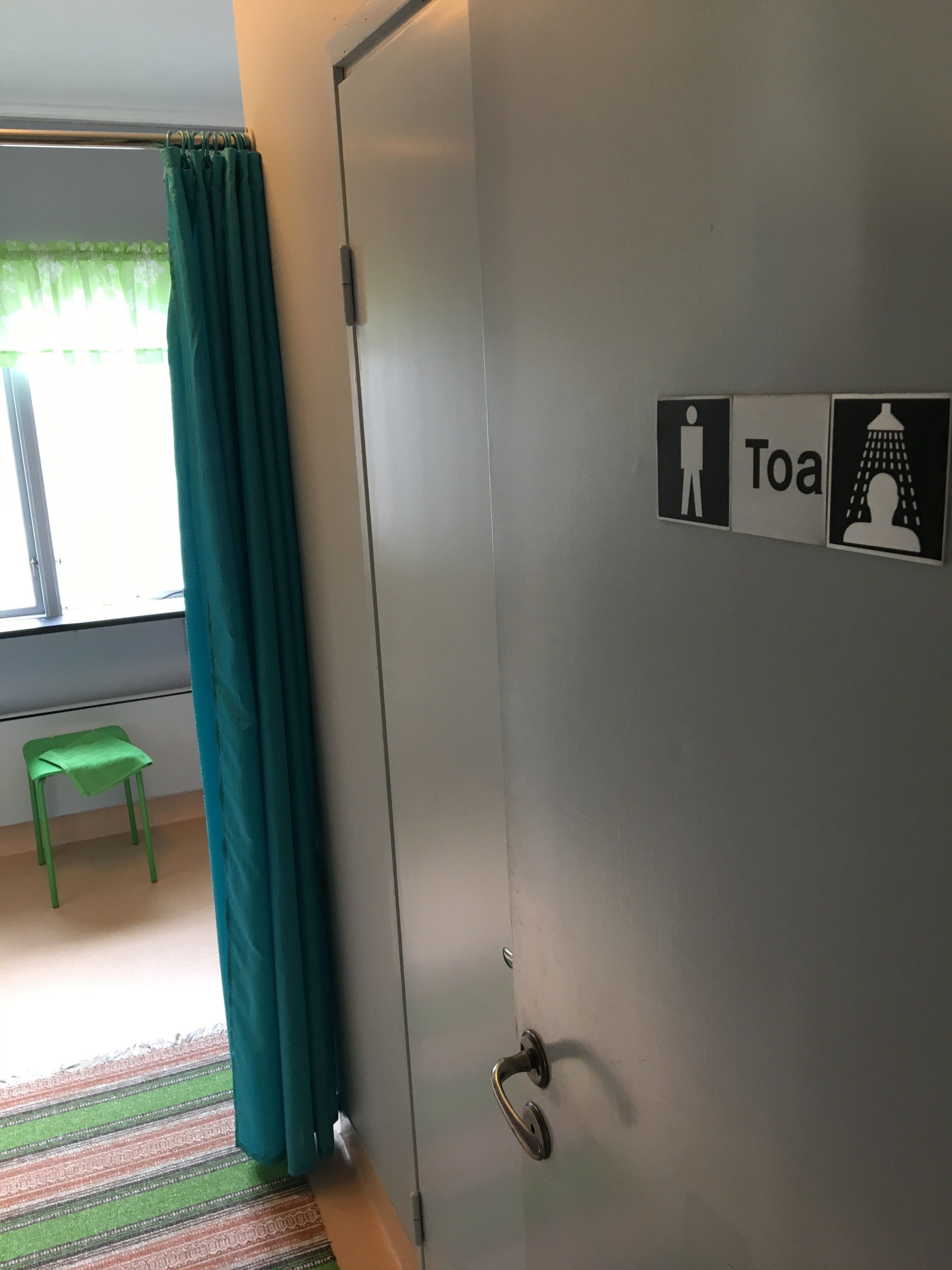 A room with a door marked "Toa" for the toilet, a green chair, and a striped rug.