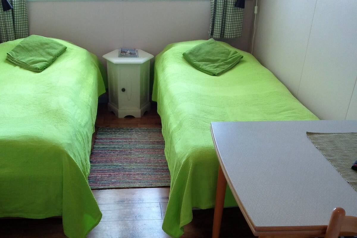 A small room with two single beds, a small table, and a chair.