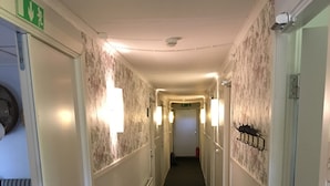 Ein Hotelgang mit strukturiertem Wandpapier, Wandleuchten und einem Feuerlöscher.