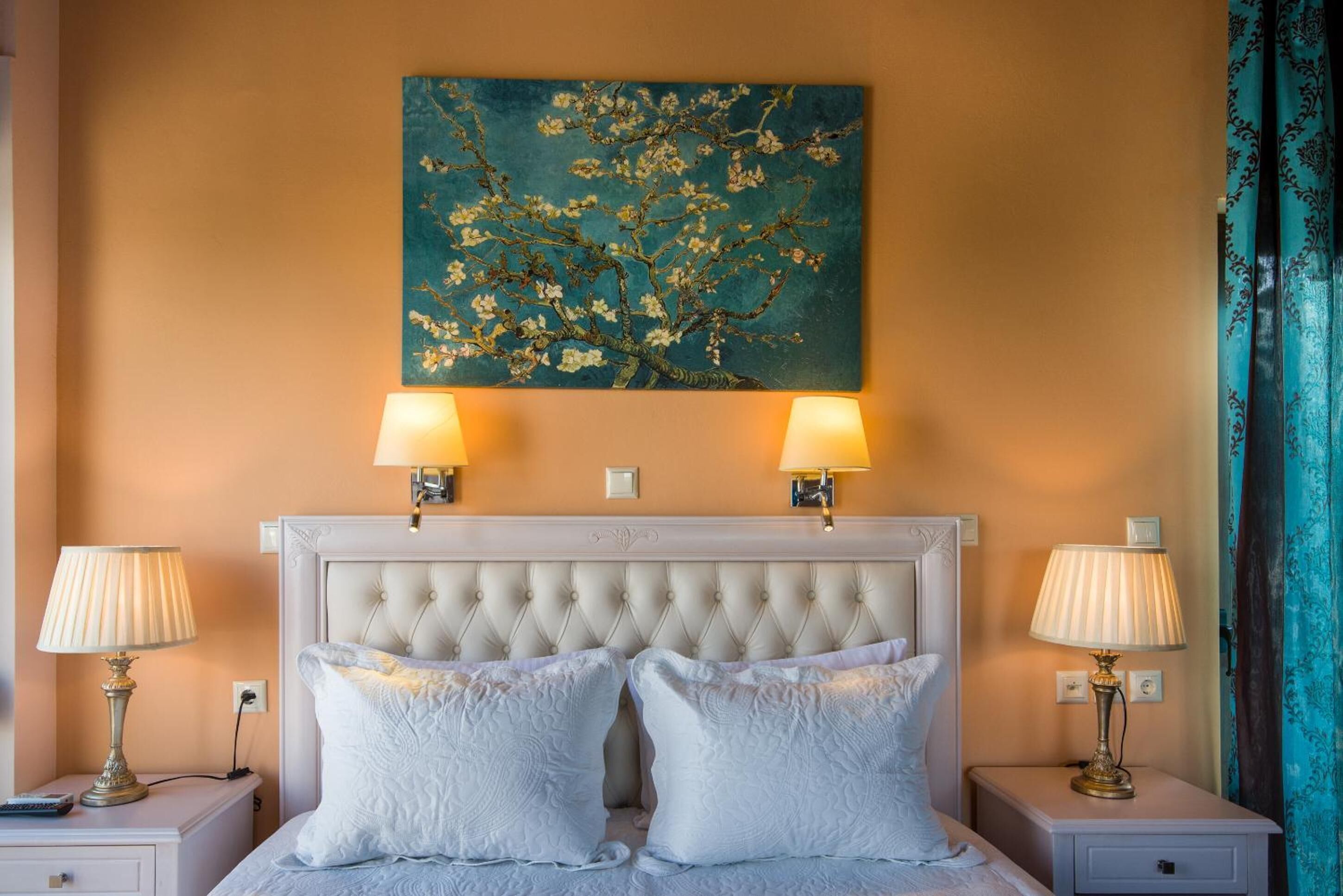 A hotel room with a tufted headboard, two bedside lamps, a painting of flowers, and a bed with white linens.