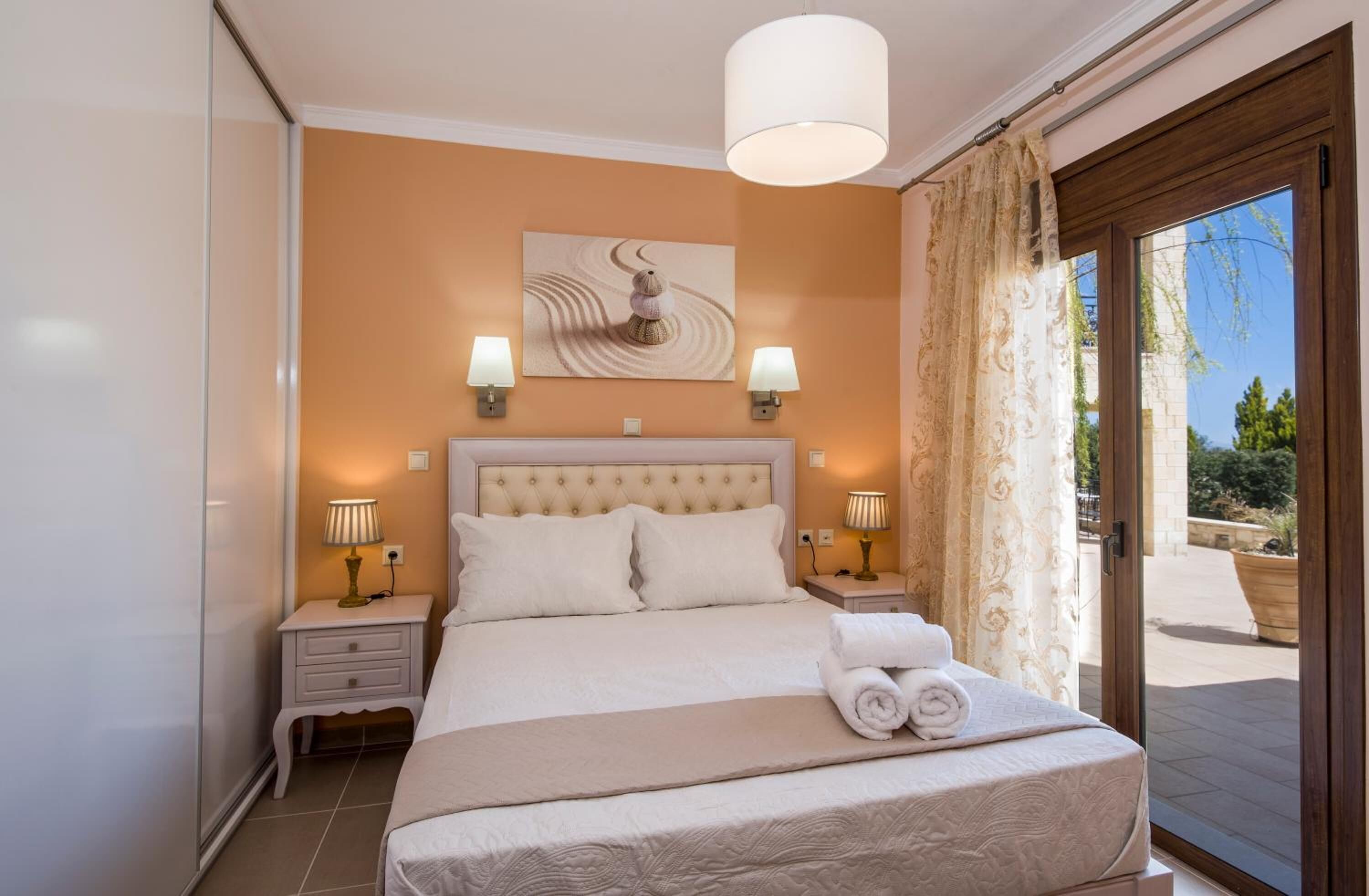 Quarto com cama grande, duas luminárias de cabeceira, luz no teto e vista para o exterior através de uma porta de vidro deslizante.