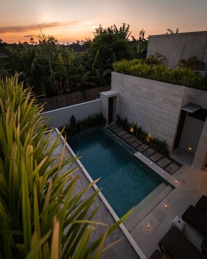 A modern outdoor pool area with a concrete edge, surrounded by lush greenery and a white wall. - Villa Portsea (Seminyak)