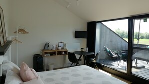 Een slaapkamer met een groot bed, een bureau met stoel, een televisie en een balkon met buitenmeubilair.